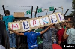 Migrants hold a banner reading "Merkel" in front of a barrier at the border with Hungary near the village of Horgos, Serbia, Sept. 16, 2015.