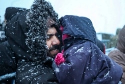 FILE - A migrant holds his child as he waits to get meal during a snowfall outside a logistics center at the checkpoint "Kuznitsa" at the Belarus-Poland border near Grodno, Belarus, Nov. 23, 2021.