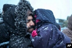 A migrant holds his child as he waits to get meal during a snowfall outside a logistics center at the checkpoint "Kuznitsa" at the Belarus-Poland border near Grodno, Belarus, Tuesday, Nov. 23, 2021.