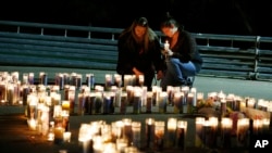 Meriah Calvert, left, and an unidentified woman pray by candles spelling out the initials for Umpqua Community College after a candlelight vigil, Roseburg, Ore., Oct. 1, 2015.