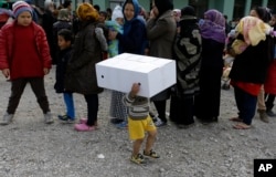 A boy plays with a cardboard box as migrants from Afghanistan wait in queues to receive food distributed by the Greek army at a refugee camp in the western Athens suburb of Schisto, March 17, 2016.