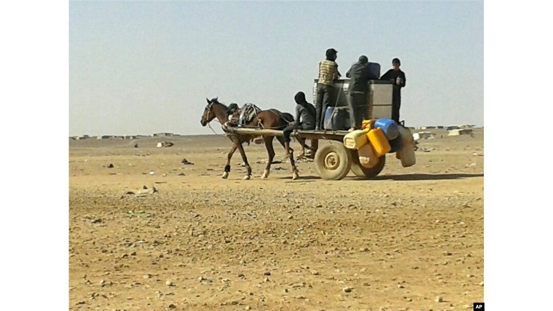 FILE - Syrian refugees ride a donkey cart full of water bottles at the Ruqban border camp, June 25, 2016.