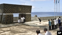 FILE - Emperor Akihito, top right, and Empress Michiko, top left, offer flowers in front of a memorial for Japanese victims on Pelelilu island in Palau April 9, 2015.