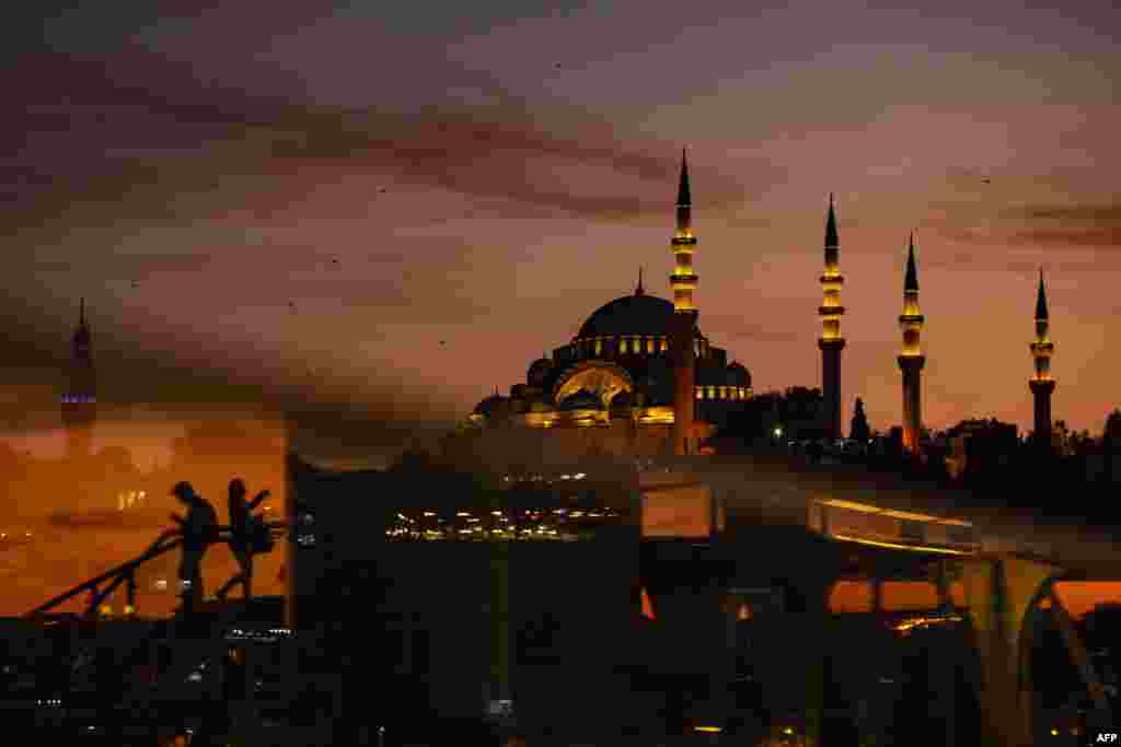 People cross the Halic bridge over the Golden Horn as Suleymaniye mosque is seen in the background during sunset over the historical Eminonu district in Istanbul, Turkey, Nov. 2, 2019.