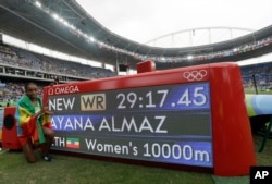 Ethiopia's Almaz Ayana poses next to a scoreboard showing her new world record in the women's 10,000-meter final during the Summer Olympics in Rio de Janeiro, Brazil, Friday, Aug. 12, 2016.
