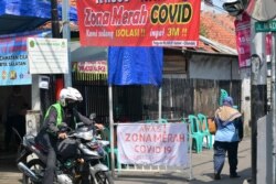 Seorang pengendara sepeda motor melewati sebuah kampung di Jakarta, yang diisolasi setelah beberapa warganya terpapar virus COVID-19, 22 Juni 2021. (Foto: BAY ISMOYO / AFP)