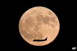 In this Nov. 14, 2016 photo, a jet plane flies across the moon which is at its brightest in almost 69 years.