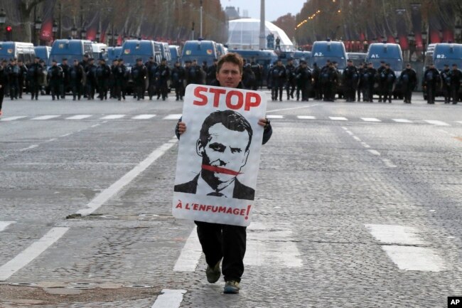 A demonstrator holds a portrait of France's President Emmanuel Macron during a protest on Paris' famed Champs-Elysees Avenue, France, Saturday, Dec. 8, 2018.