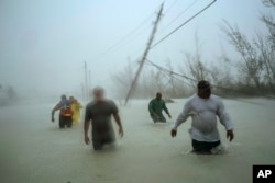 Volunteers walk under the wind and rain from Hurricane Dorian through a flooded road as they work to rescue families near the Causarina bridge in Freeport, Grand Bahama, Bahamas, Tuesday, Sept. 3, 2019.