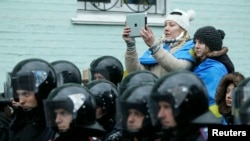 FILE - A supporter of the pro-presidential Party of the Regions takes pictures of a rally to support EU integration, with riot police and Interior Ministry personnel blocking a street in the foreground, in central Kyiv, December 2013.