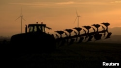 FILE - A French farmer drives a tractor as he ploughs a field in front of power-generating windmill turbines at a wind park in Vauvillers, in France, November 23, 2015. A new study counts farms among the biggest contributors to pollution.