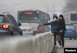 FILE - A woman wearing a mask waits for a taxi on a heavy hazy day in Beijing.