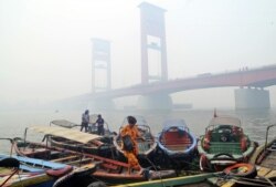 Seorang perempuan di atas perahu di dekat Jembatan Ampera, Palembang yang diselimuti kabut asap kebakaran hutan, Palembang, Sumatera Selatan, 29 September 2015. (Foto: AP)