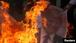 A Palestinian protester burns a poster depicting U.S. President Donald Trump during a protest against Trump's decision to recognize Jerusalem as the capital of Israel, in Gaza City, Dec. 7, 2017.