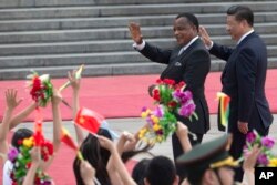 FILE - Chinese President Xi Jinping, right and Republic of Congo President Denis Sassou Nguesso wave as they walk past Chinese children waving flags and flowers to welcome them at a welcome ceremony held outside the Great Hall of the People in Beijing, China, July 5, 2016.