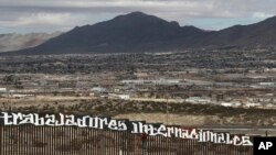 Sunland Park, New Mexico, is seen over the U.S. border fence as a protester finishes painting the Spanish slogan "Neither delinquents nor illegals, we are international workers" on the Anapra, Mexico, side of the fence, Feb. 26, 2017. 