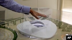 FILE- In this photo taken during a government-organized media tour, an official makes a point using a scale model of the Al-Wakra Stadium, to be used during the 2022 World Cup, in Doha, Qatar, May 4, 2015.