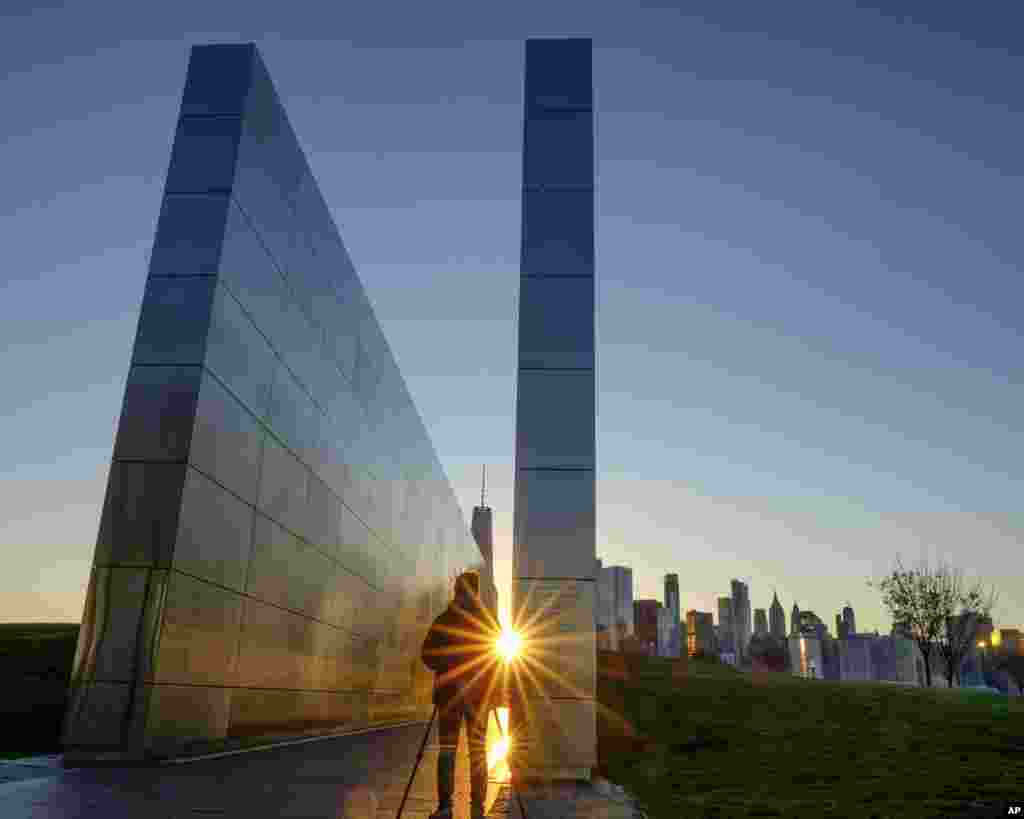 The light reflects off of the Empty Sky Memorial in Jersey City, New Jersey, as the sun rises over the New York City skyline.