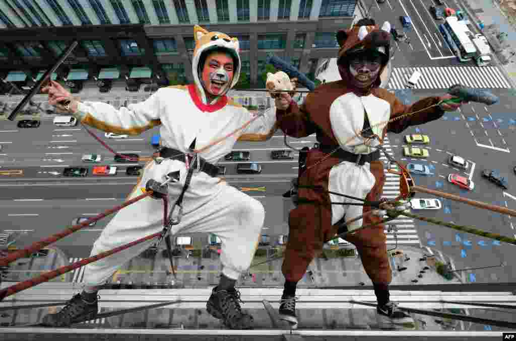 Workers clad in dog (left) and wild boar costumes, respectively, to represent the outgoing year of the dog and incoming year of the wild boar, clean windows on the side of a hotel in Tokyo, Japan.