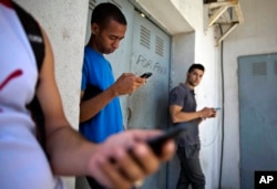FILE - Students gather behind a business looking for an Internet signal for their smartphones in Havana, Cuba, April 1, 2014.