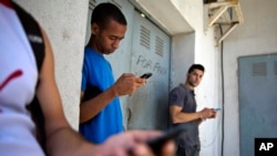 FILE - Students gather behind a business looking for a Internet signal for their smart phones in Havana, Cuba, April 1, 2014. 