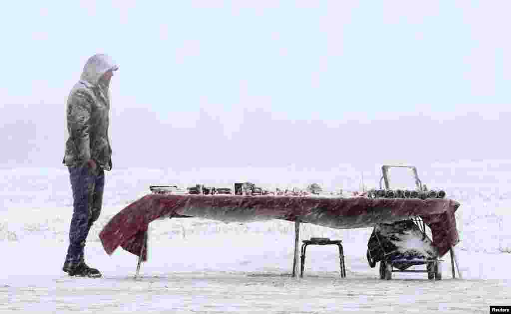 A street vendor selling souvenirs waits for customers during a snow fall in the Aziarco village, Belarus, Feb. 25, 2017.