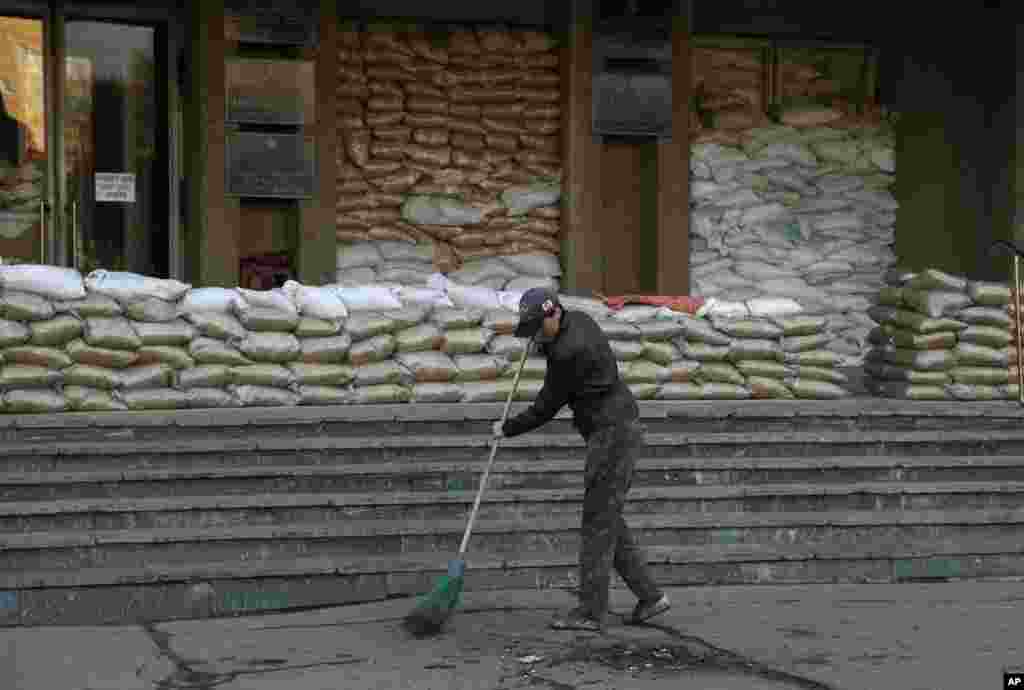 A woman cleans up trash in front of an entrance to a city administration building in Slovyansk, Ukraine, April 16, 2014.