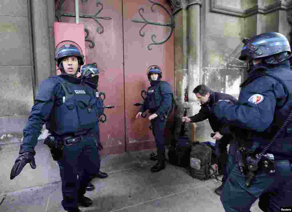 French police stand at the door of the Eglise Neuve church as they secure the area during an operation in Saint-Denis, near Paris, to catch fugitives from Friday night's deadly attacks in Paris, Nov. 18, 2015.