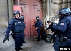 French police stand at the door of the Eglise Neuve church as they secure the area during an operation in Saint-Denis, near Paris, to catch fugitives from Friday night's deadly attacks in Paris, Nov. 18, 2015.