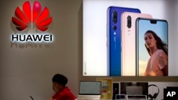 A sales clerk looks at his smartphone in a Huawei store at a shopping mall in Beijing Wednesday, July 4, 2018. 