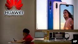 ພະ​ນັກ​ງານ​ຂາຍ​ໂທ​ລະ​ສັບ​ສະ​ຫລ​າດ ຫລື smartphone ຢູ່​ຮ້ານ​ຂາຍ​ໂທ​ລະ​ສັບ Huawei ​ຢູ່​ເຂດ​ຫ້າງ​ຂາຍ​ສິນ​ຄ້າ​ໃຫຍ່​ແຫ່ງ​ນຶ່ງ​ໃນ​ນ​ພ​ຄອນ​ປັກ​ກິ່ງ (ພາບ​ຖ່າຍ​ໃນ​ວັນ​ທີ 4 ກໍ​ລະ​ກົດ, 2018) 