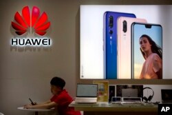 FILE - A salesclerk looks at his smartphone in a Huawei store at a shopping mall in Beijing, July 4, 2018.