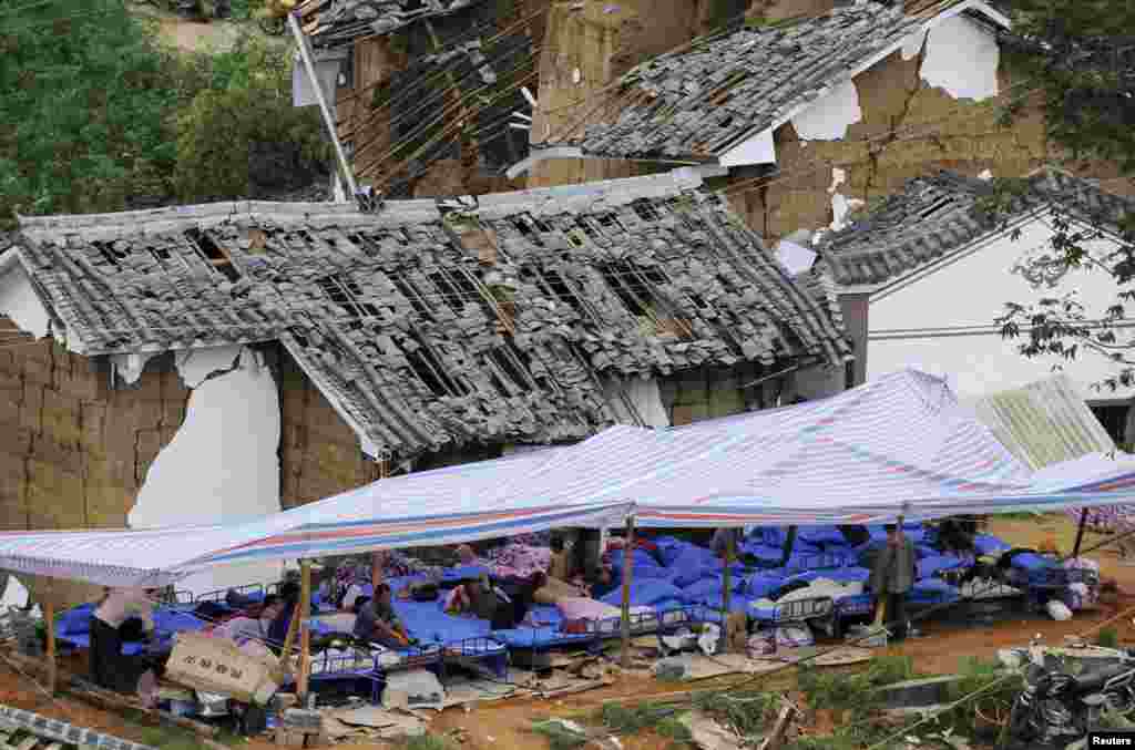 8月4日，一些村民坐在应急帐篷下休息。他们旁边是被地震损毁的房屋。
