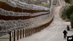 Un niño anda en bicicleta junto al muro fronterizo que separa a Nogales, Arizona, de Nogales, México, al otro lado, el sábado 2 de marzo de 2019. (AP Foto/Charlie Riedel)