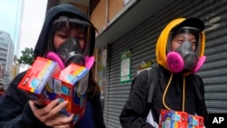 Citizens wearing full mask respirators carry packets of disposable face masks in Hong Kong, Wednesday, Feb. 5, 2020. (AP Photo/Vincent Yu)