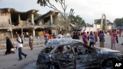 Raia wa somalia wakitembea karibu na jengo lililoharibiwa na milipuko.
