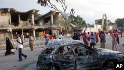 Warga Somalia berjalan melewati bangunan dan mobil yang hancur akibat serangan bom bunuh diri di Mogadishu, Somalia (27/2).