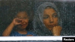 FILE - Migrants look out through the window of a train at the railway station in Bicske, Hungary, Sept. 4, 2015.