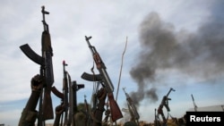 FILE - Rebel fighters hold up their rifles as they walk in front of a bushfire in a rebel-controlled territory in Upper Nile State, South Sudan February 13, 2014.