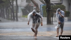 日本遭受颱風黃蜂襲擊，沖繩島兩名居民抵禦強風走上街上。