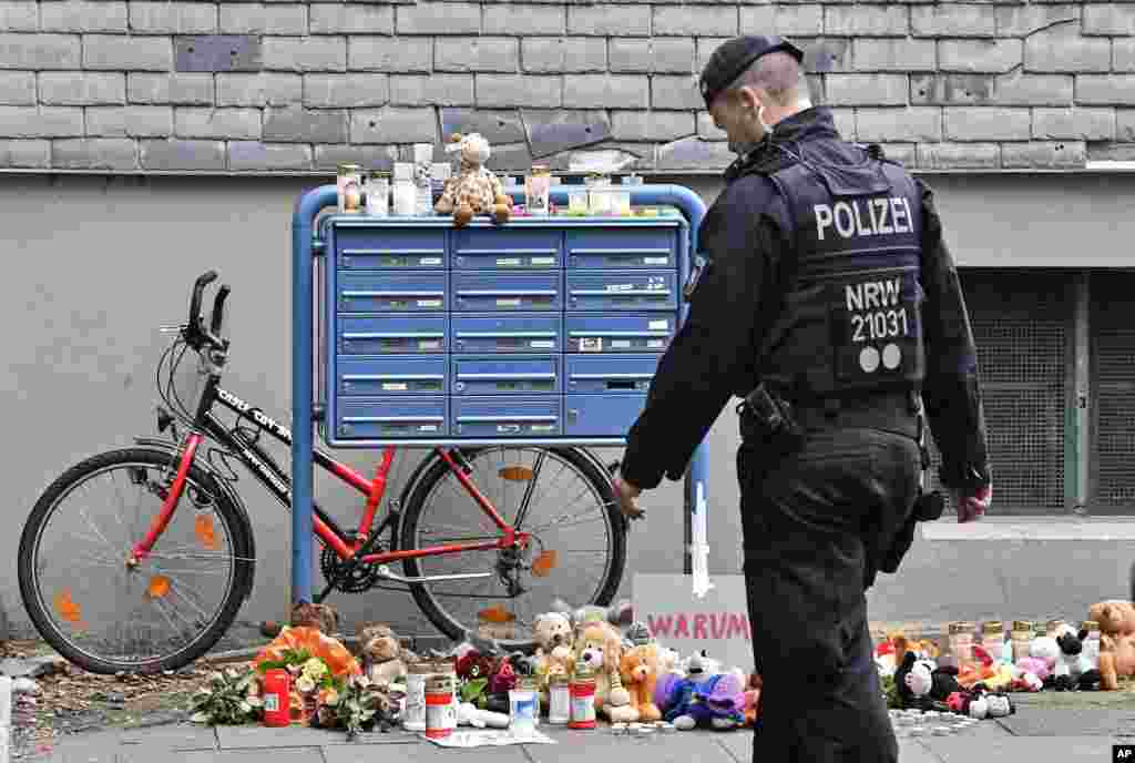 A police officer passes candles and teddy bears at the entrance of a house where five dead children were found in Solingen, Germany. The children&#39;s mother is suspected in the deaths.