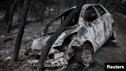 Sebuah kerangka mobil yang terbakar terjebak di bawah pohon yang terbakar menyusul kebakaran lahar di Neos Voutzas, dekat Athena, Yunani, 26 Juli 2018.