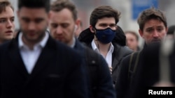 Para pekerja, beberapa mengenakan masker, menyeberangi Jembatan London, saat jam sibuk di London, 5 Maret 2020. (Foto: Reuters)