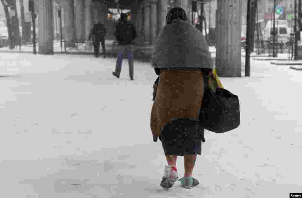 A homeless woman, her feet wrapped in plastic, walks in the snow in Paris as winter weather with snow and freezing temperatures returns to northern France. 