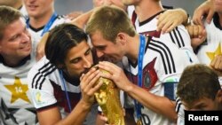 Germany's Sami Khedira (L) and Philipp Lahm (2nd R) kiss the World Cup trophy as they celebrate at the end of the 2014 World Cup final between Germany and Argentina at the Maracana stadium in Rio de Janeiro, July 13, 2014.