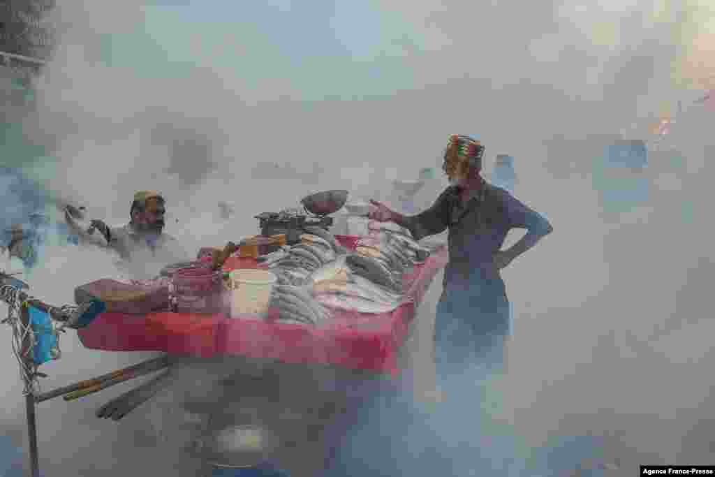 People selling fish stand next to their cart during a fumigation drive as a preventive measure against disease-carrying mosquitoes, in Karachi, Pakistan, Oct. 26, 2021.