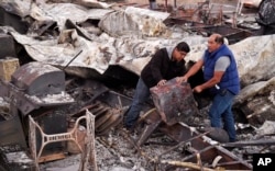 Santos Alvarado, right, and his son Ricky recover a safe deposit box from their destroyed home at Seminole Springs Mobile Home Park, Sunday, Nov. 11, 2018, following devastating wildfires in the area in Agoura Hills, Calif. (AP Photo/Chris Pizzello)