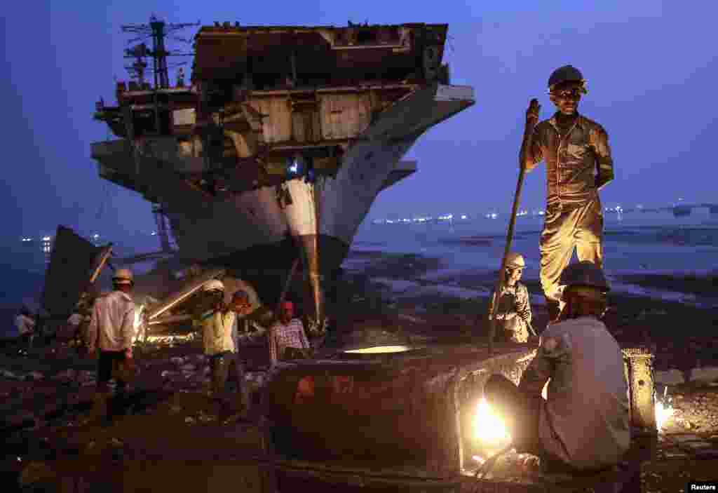 A worker uses a metal cutter as others carry to the dismantled parts of a decommissioned Indian Navy Ship INS Vikrant at a ship breaking yard in Mumbai.