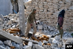 Fighters of the U.S.-backed Kurdish-led Syrian Democratic Forces walk through debris and mortar shells in the village of Baghuz in the eastern Syrian province of Deir Ezzor on March 21, 2019.