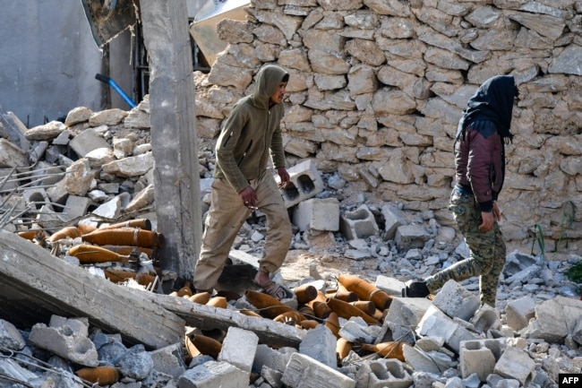 Fighters of the U.S.-backed Kurdish-led Syrian Democratic Forces walk through debris and mortar shells in the village of Baghuz in the eastern Syrian province of Deir Ezzor on March 21, 2019.